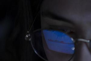 jeune femme, regardant la bourse la nuit, le même marché se voit dans le reflet de ses lunettes photo