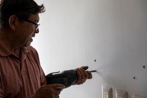 homme latino utilisant une perceuse électrique pour percer des trous dans le mur pour accrocher une nouvelle télévision, percer des trous dans le mur, mexicain, hispanique photo