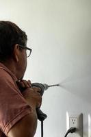 homme latin dans la cinquantaine, percer un mur avec une perceuse, mur blanc photo