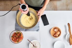 femme dans la cuisine cuisinant un gâteau. les mains battent la pâte avec un batteur électrique, vue de dessus photo