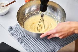 femme dans la cuisine cuisinant un gâteau. les mains battent la pâte avec un batteur électrique photo