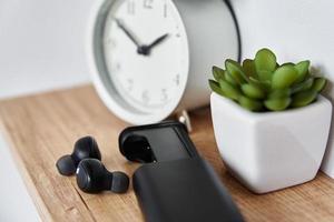 écouteurs sans fil sur étagère avec réveil et plante d'intérieur. photo