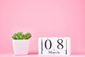 concept de la journée de la femme. bloc calendrier en bois avec date 8 mars et plante sur fond rose avec espace de copie photo