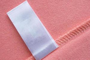 étiquette de vêtements de soin de lessive blanche vierge sur fond de texture de tissu rose photo