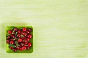 assiette verte avec des cerises fraîches et des framboises sur le fond en bois vert, vue de dessus. photo