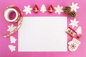 vue de dessus sur les décorations de noël, les pommes de pin et la feuille de papier blanche sur fond rose avec espace de copie. photo