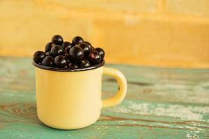 une tasse en métal orange avec du cassis sur la table en bois bleue et blanche et sur le fond du mur de briques. photo