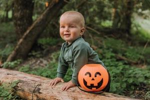 charmant petit garçon mignon avec un panier de citrouille pour les bonbons est assis sous un saule au coucher du soleil. fabuleuse belle forêt magique. notion d'Halloween. l'enfant joue à l'extérieur. espace pour le texte photo