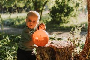 charmant petit garçon mignon avec un panier de citrouille pour les bonbons est assis sous un saule au coucher du soleil. fabuleuse belle forêt magique. notion d'Halloween. l'enfant joue à l'extérieur. espace pour le texte photo