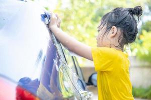 enfant asiatique mignon lavant une voiture avec un tuyau le jour d'été photo