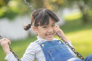 heureuse petite fille asiatique jouant à la balançoire en plein air dans le parc photo