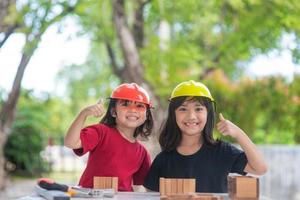 frères et sœurs asiatiques filles portant des chapeaux d'ingénierie construisant une maison à partir du jouet en bois. pour apprendre et améliorer le développement, petit architecte. photo