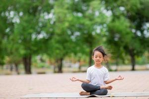 petite fille asiatique mignonne pratiquant la pose de yoga sur un tapis dans le parc, concept de santé et d'exercice photo