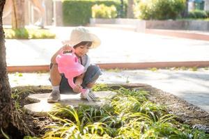 petite fille asiatique versant de l'eau sur les arbres. kid aide à prendre soin des plantes avec un arrosoir dans le jardin. photo