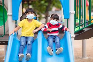 nouveau mode de vie normal, concept de distanciation sociale. des enfants heureux portant un masque facial s'amusant sur l'aire de jeux protègent le coronavirus covid-19, photo