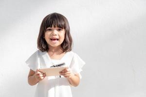 Une petite fille asiatique excitée utilise un smartphone, un espace vide tourné isolé sur fond blanc photo