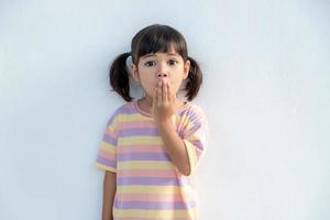 portrait d'une mignonne petite fille en bas âge surprise debout isolée sur fond blanc. regardant la caméra. mains près de la bouche ouverte photo