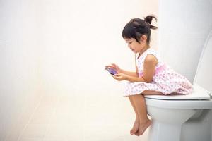 enfants asiatiques assis sur des toilettes et tenant un smartphone.