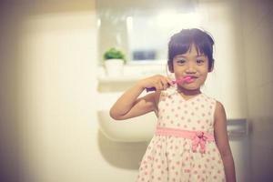 petite mignonne petite fille se nettoyant les dents avec une brosse à dents dans la salle de bain photo