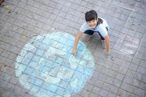 les enfants asiatiques jouent à l'extérieur. une enfant fille dessine un globe terrestre avec une carte du monde à la craie colorée sur le trottoir, l'asphalte. terre, concert du jour de la paix. photo