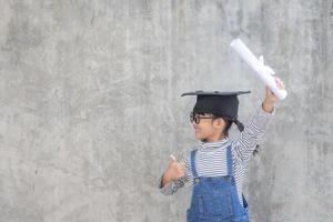 petite fille asiatique portant un bonnet de graduation et titulaire d'un diplôme sur fond blanc photo