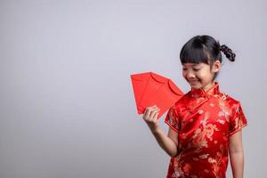 heureuse petite fille asiatique en costume traditionnel chinois souriant et tenant une enveloppe rouge. concept de joyeux nouvel an chinois. photo