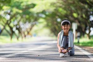 enfant attachant des chaussures de course. heureuse drôle petite fille asiatique fitness femme courant le matin. jeune enfant athlétique courant dans la nature. mode de vie sain photo