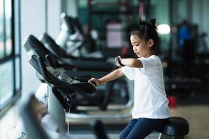 une petite fille regarde une montre intelligente après s'être entraînée en salle de sport. notion saine. la femme après la séance d'entraînement vérifie les résultats sur la montre. photo