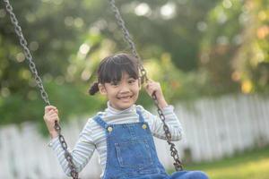 heureuse petite fille asiatique jouant à la balançoire en plein air dans le parc photo