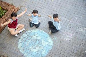les enfants asiatiques jouent à l'extérieur. une enfant fille dessine un globe terrestre avec une carte du monde à la craie colorée sur le trottoir, l'asphalte. terre, concert du jour de la paix.