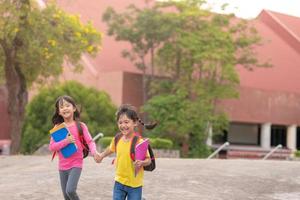 retour à l'école. deux jolies filles asiatiques avec sac d'école tenant un livre et marchant ensemble à l'école photo