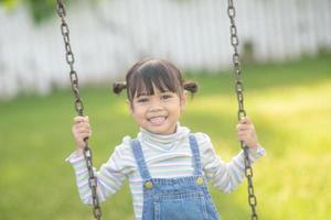 heureuse petite fille asiatique jouant à la balançoire en plein air dans le parc photo