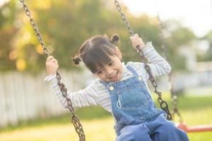 heureuse petite fille asiatique jouant à la balançoire en plein air dans le parc photo