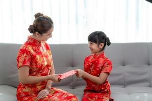 une petite fille asiatique heureuse a reçu une enveloppe rouge de sa mère pour le nouvel an chinois photo