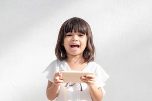 Une petite fille asiatique excitée utilise un smartphone, un espace vide tourné isolé sur fond blanc photo