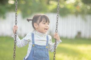 heureuse petite fille asiatique jouant à la balançoire en plein air dans le parc photo