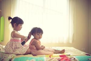 jolie petite fille se brosser les cheveux de sa sœur alors qu'il était assis sur le lit photo