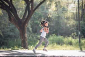 fille enfant heureuse qui court dans le parc en été dans la nature. lumière du soleil chaude. le petit asiatique court dans un parc. sports de plein air et fitness, apprentissage de l'exercice et de la compétition pour le développement des enfants. photo