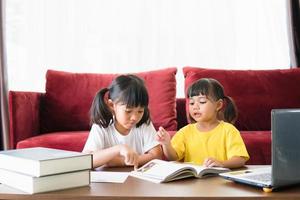 deux étudiantes asiatiques étudient en ligne avec l'enseignant par appel vidéo ensemble. les frères et sœurs font l'école à la maison avec un ordinateur portable pendant la quarantaine en raison de la pandémie de covid 19. photo