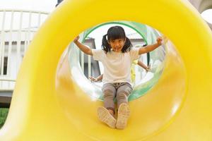 enfant jouant sur une aire de jeux extérieure. les enfants jouent dans la cour de l'école ou de la maternelle. enfant actif sur un toboggan et une balançoire colorés. activité estivale saine pour les enfants. photo