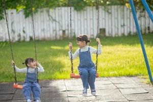 deux jolies petites soeurs s'amusant ensemble sur une balançoire dans un beau jardin d'été par une journée chaude et ensoleillée à l'extérieur. loisirs d'été actifs pour les enfants. photo