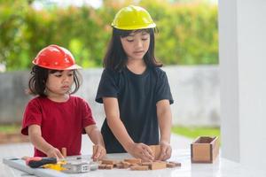 frères et sœurs asiatiques filles portant des chapeaux d'ingénierie construisant une maison à partir du jouet en bois. pour apprendre et améliorer le développement, petit architecte. photo