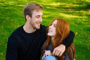 heureux jeune couple assis dans une étreinte dans le parc sur l'herbe photo