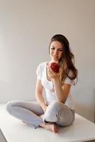 belle femme caucasienne décontractée est sur le point de mordre une pomme dans la cuisine, un jeune photo