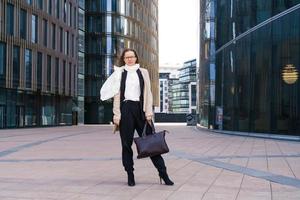 femme réussie avec des lunettes se tient devant un immeuble de bureaux avec sac photo