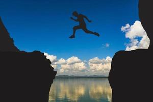 une silhouette d'un homme sautant par-dessus une falaise sur le chemin de la victoire. photo