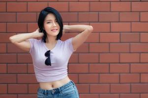 portrait de fille hipster sur fond de mur de briques, belle femme asiatique pose pour prendre une photo