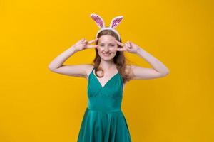 jolie fille positive posant avec des oreilles de lapin et en robe verte sur jaune photo