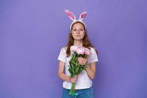 Jolie jeune femme avec des oreilles de lapin de Pâques rose sur fond violet en blanc photo