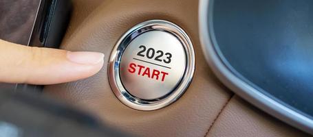 doigt appuyez sur un bouton d'allumage de voiture avec le texte de démarrage 2023 à l'intérieur de l'automobile. nouvel an nouveau vous, prévision, résolution, motivation, changement, objectif, vision, innovation et concept de planification photo